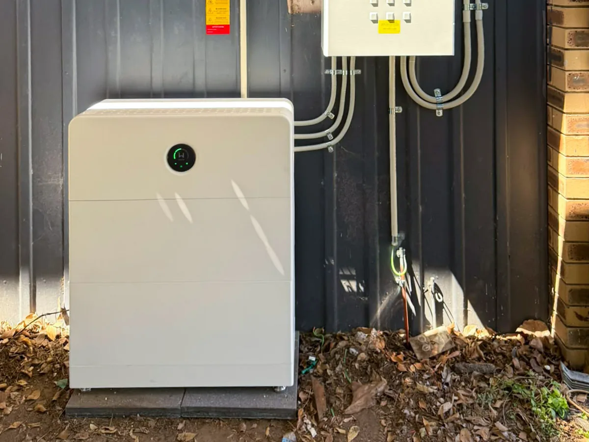 A home battery installed by EFS Solar against a dark corrugated wall in Alexandra Hills, beside the backup switchboard