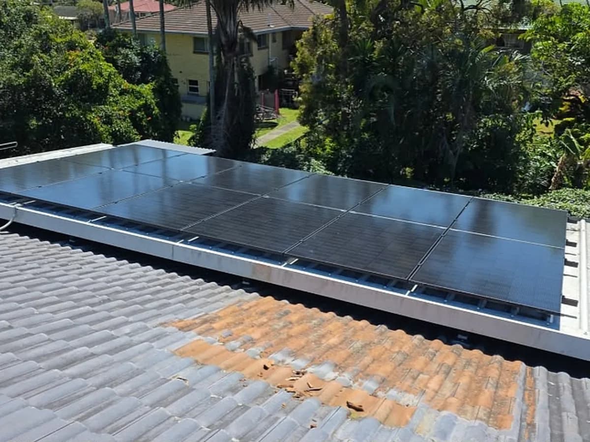 A row of black solar panels along a low-set roof in Alexandra Hills, with a Queenslander behind