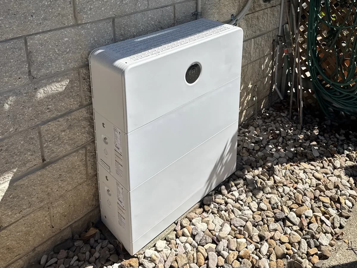 A home battery installed by EFS Solar against a block wall in Biggera Waters, set on a bed of river stones