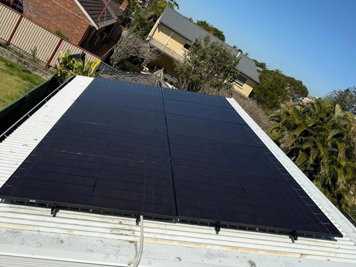 Black solar panels on a white metal roof in Boondall, looking out over the neighbouring rooftops and palms