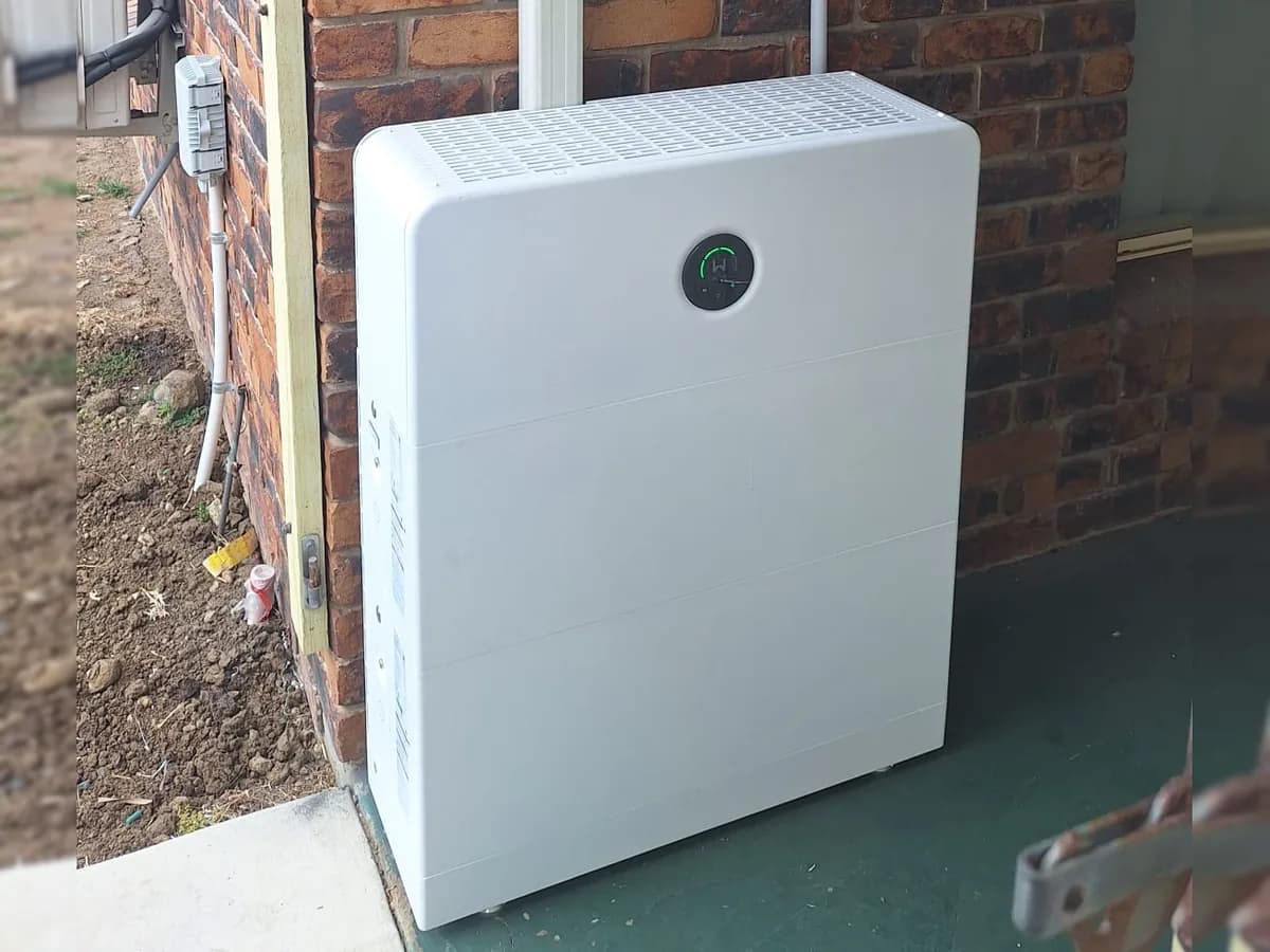 A home battery installed by EFS Solar against a brick wall in Bundaberg East, with its conduits running up the wall