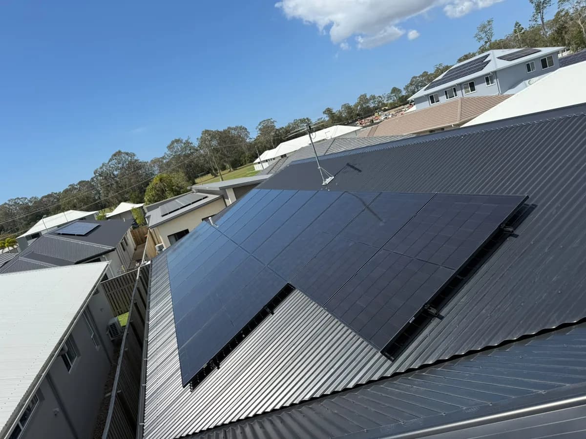 Black solar panels across a dark metal roof in Burpengary East, with the new estate rooftops and gum trees beyond