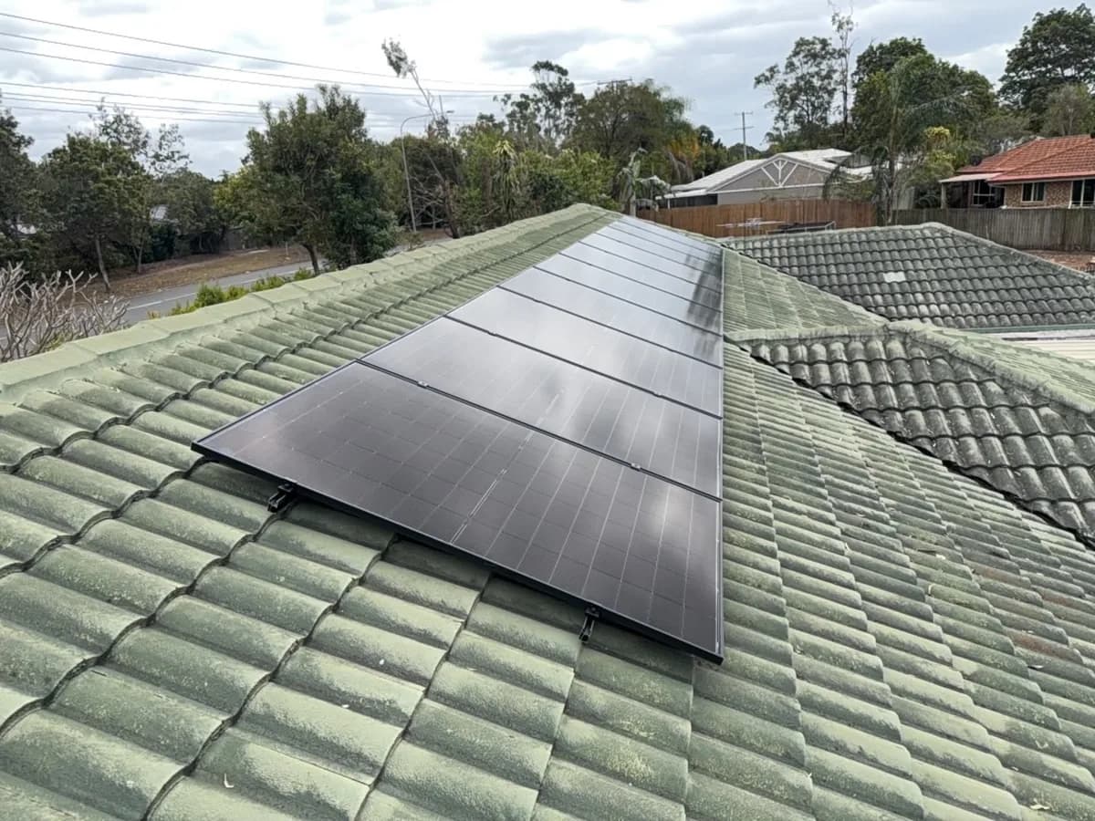 Black solar panels on the green-tiled roof of a Camira home, with the street and gum trees behind