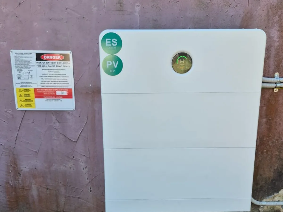 A home battery installed by EFS Solar against a rendered wall in Eaton, near Gladstone, beside the isolators and shutdown signage