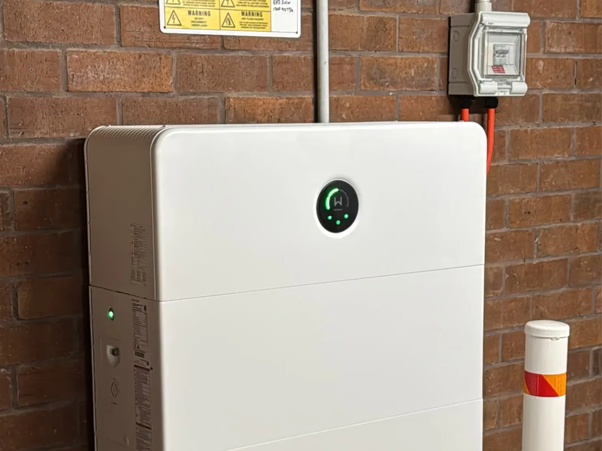 A home battery installed by EFS Solar against a red brick wall at Gladstone, near Kempsey, with a protective bollard and shutdown signage