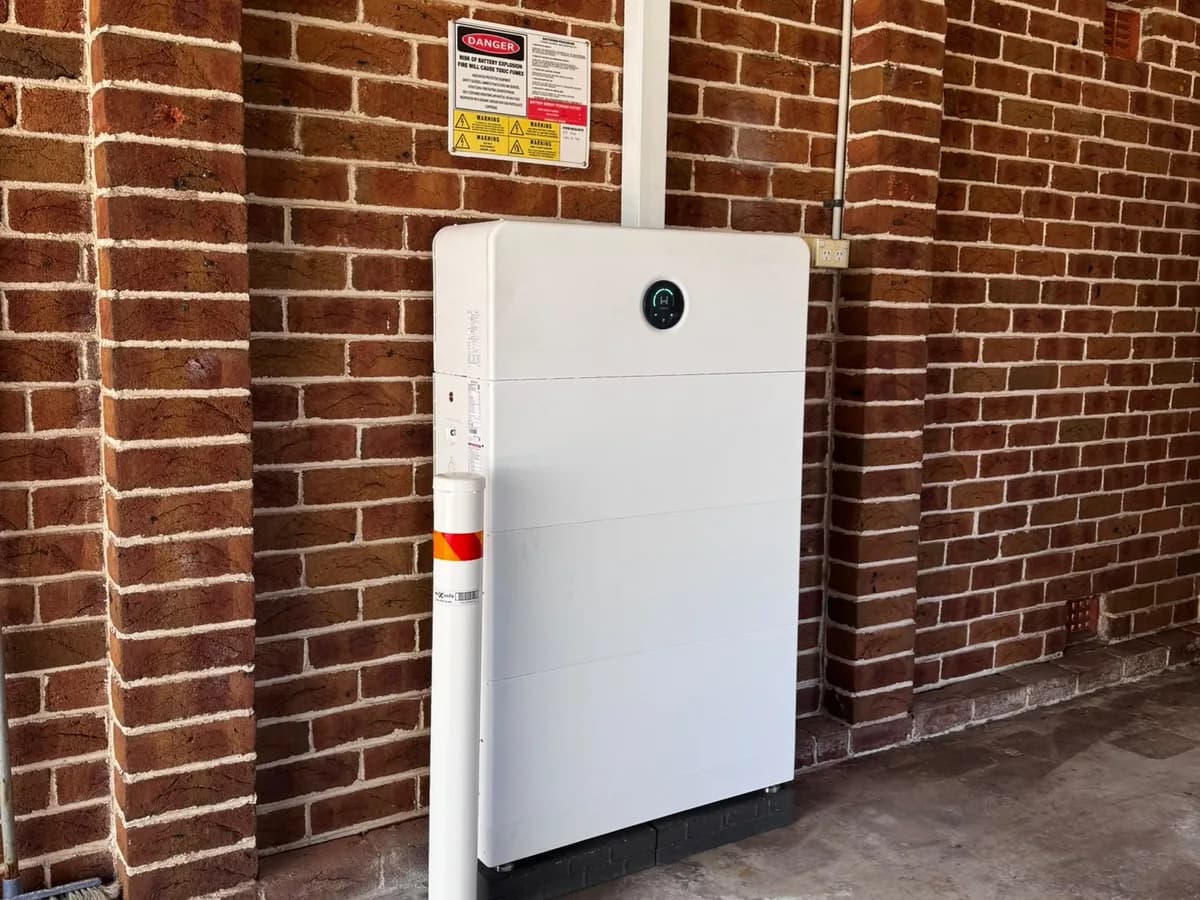 A home battery installed by EFS Solar against a red brick wall in Helensburgh, with a protective bollard and shutdown signage