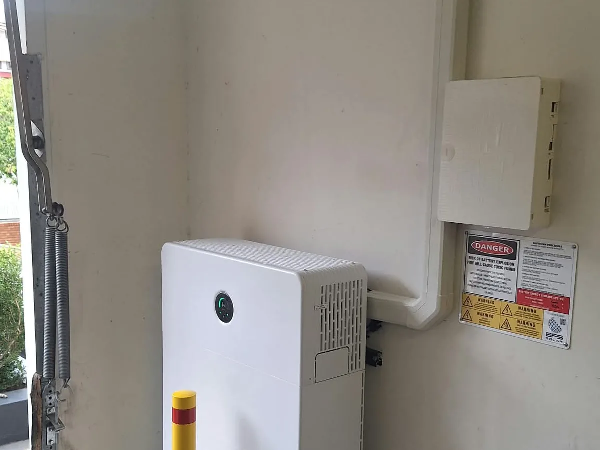 A home battery installed by EFS Solar in a Highgate Hill garage, with a protective bollard and shutdown signage