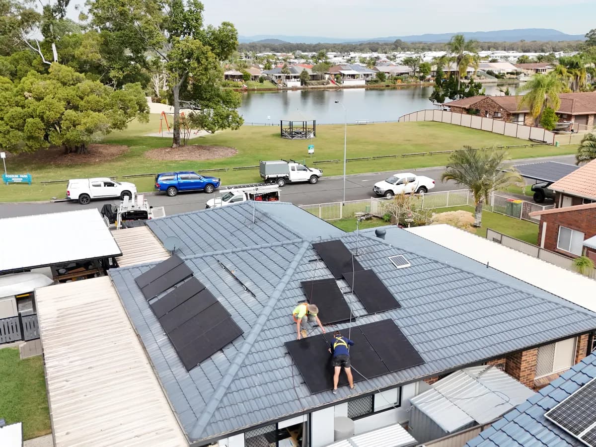 Solar installation in Hollywell — two installers laying panels across a tiled roof opposite a local park and waterway