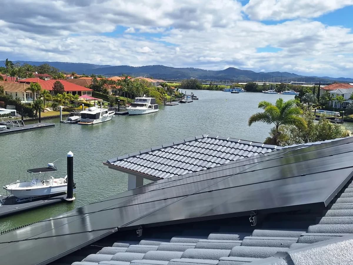Black solar panels on a dark-tiled roof at a Hope Island canal home, looking out over the waterway, moored boats and the hinterland