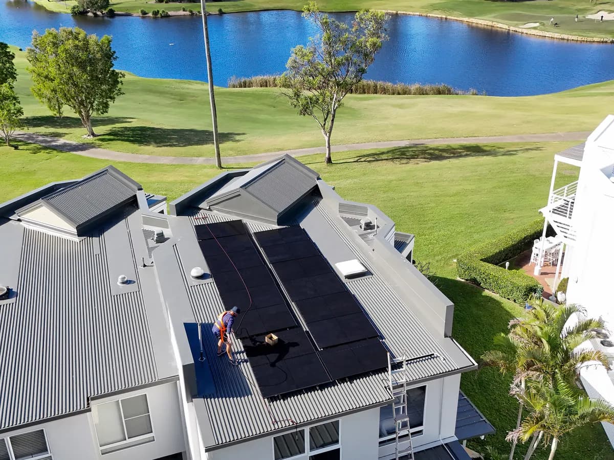 Solar installation in Hope Island — a metal roof being fitted with solar, backing onto a golf course and lake