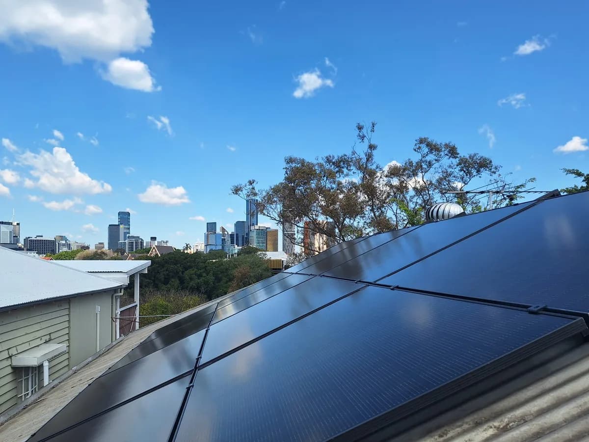 Black-on-black panels on a Kelvin Grove rooftop with the Brisbane city skyline on the horizon behind