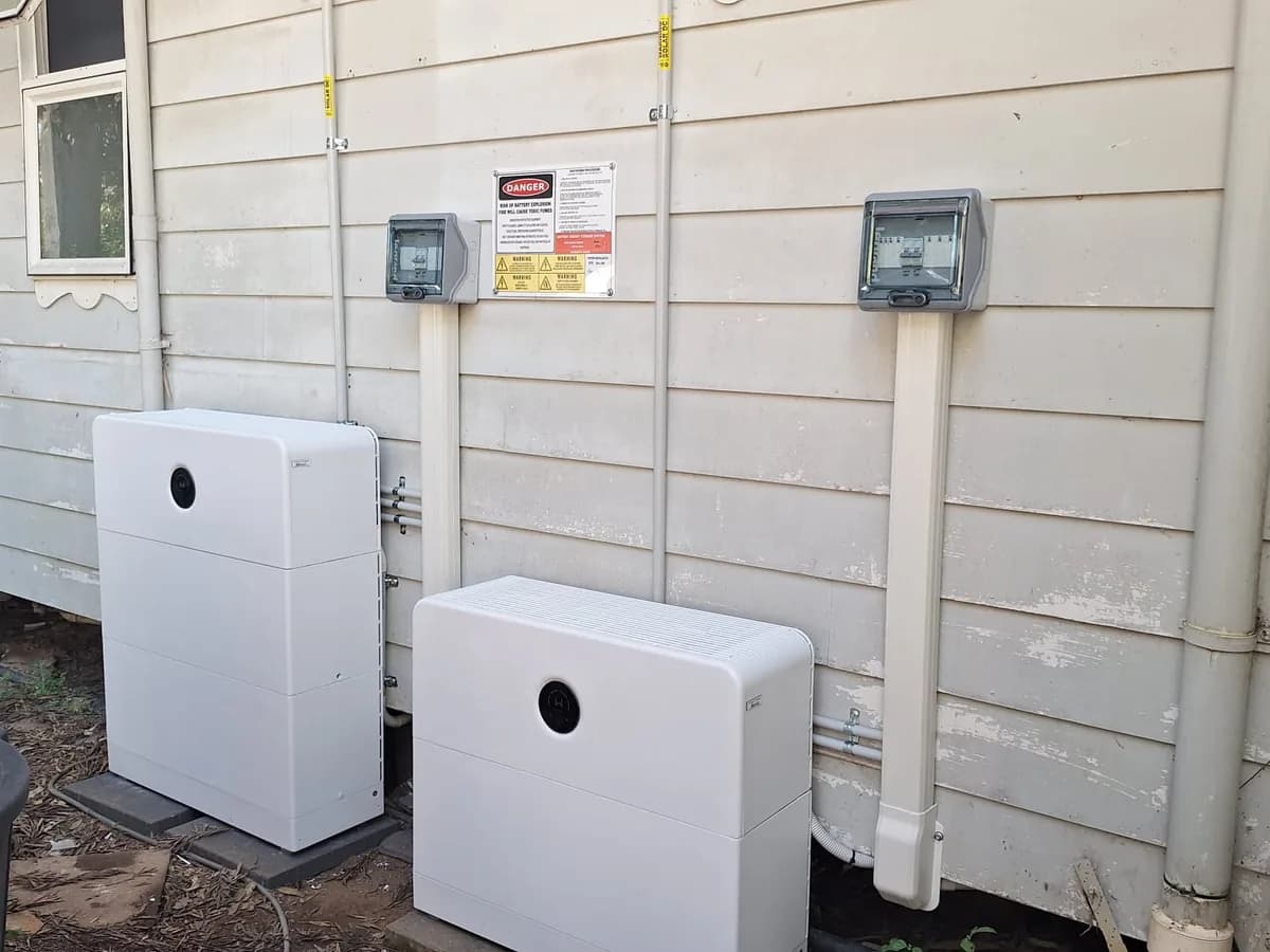 Two home battery units installed by EFS Solar along a weatherboard wall in Kin Kin, with isolators and signage above