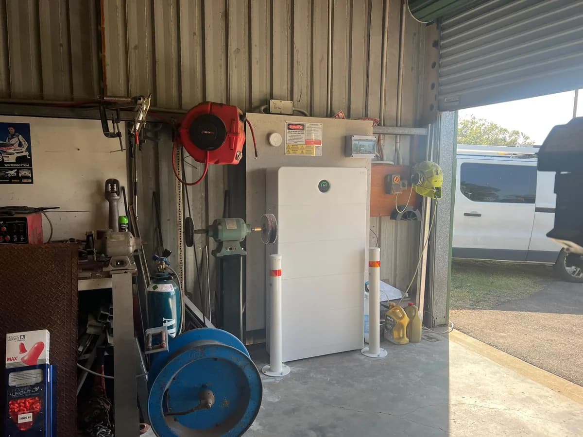 A home battery installed by EFS Solar in a Medowie workshop, flanked by safety bollards, with the switchboard and shutdown signage above
