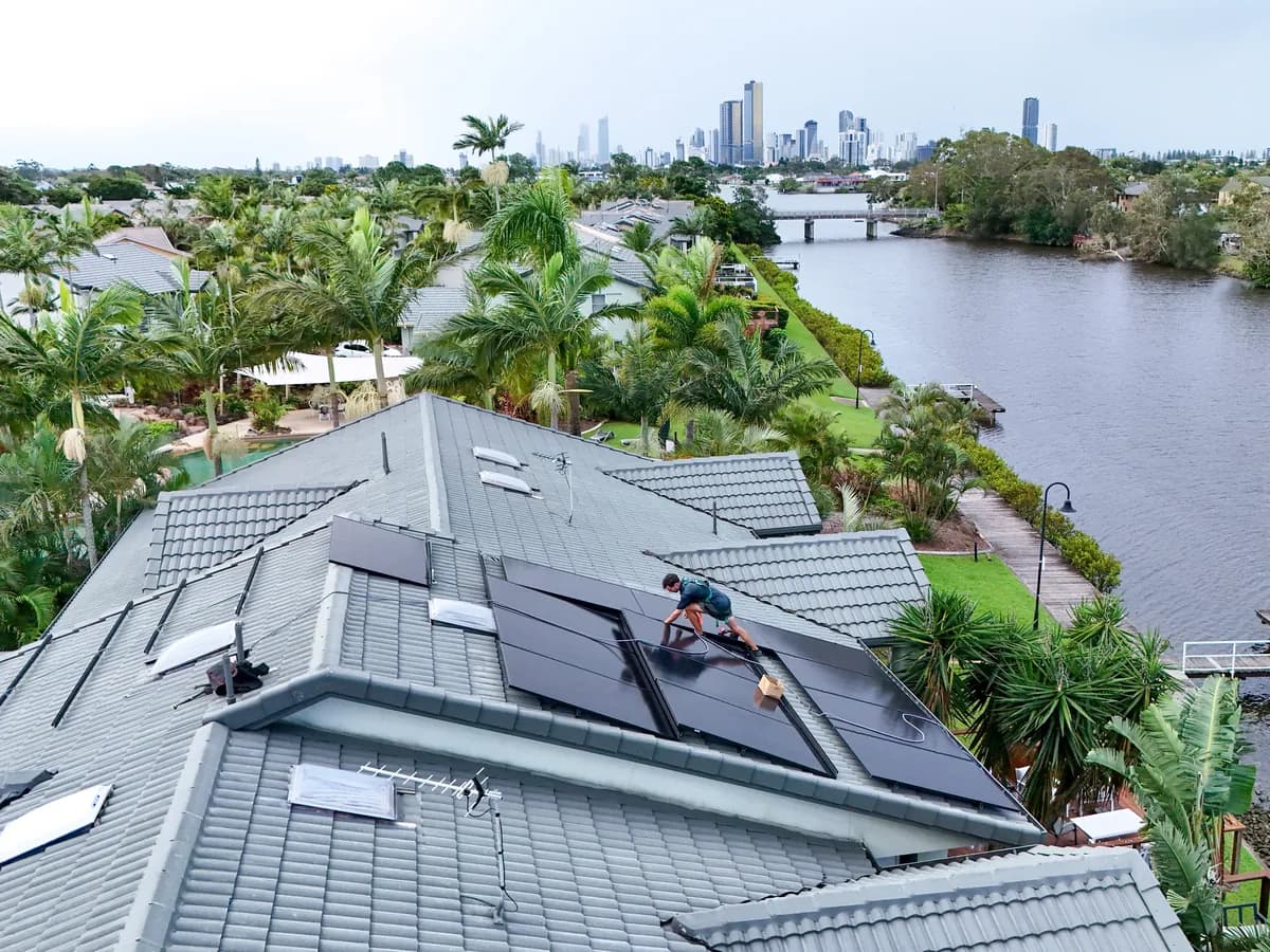 Solar installation in Mermaid Waters — a waterfront tiled roof being fitted with solar, looking across the canal to the city skyline