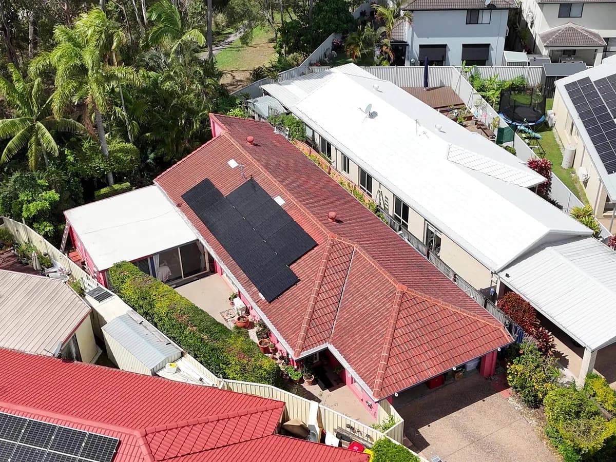 Aerial view of black solar panels on the red-tiled roof of a Molendinar home, backing onto bushland