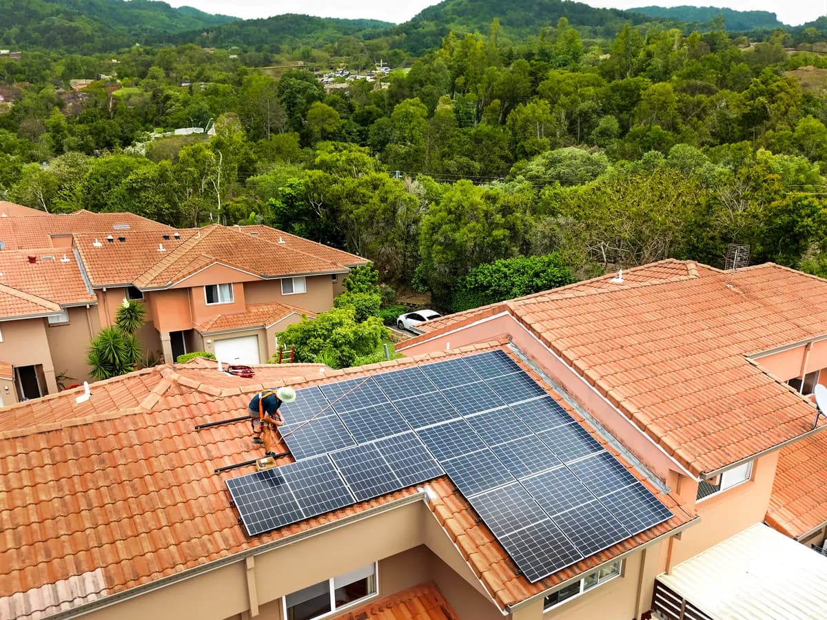 Solar installation in Nerang — panels going on to a terracotta tiled roof with the hinterland ranges behind
