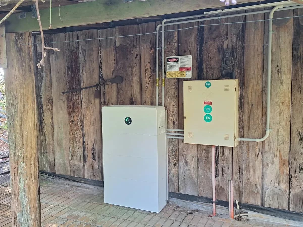 A home battery installed by EFS Solar against a timber slab wall at a North Maleny property, beside the PV and battery isolators