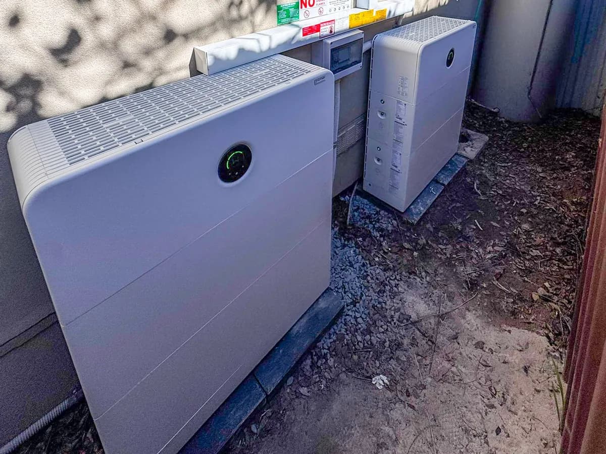 Two home battery units and an inverter installed by EFS Solar along a rendered wall in Singleton Heights, dappled with tree shadow