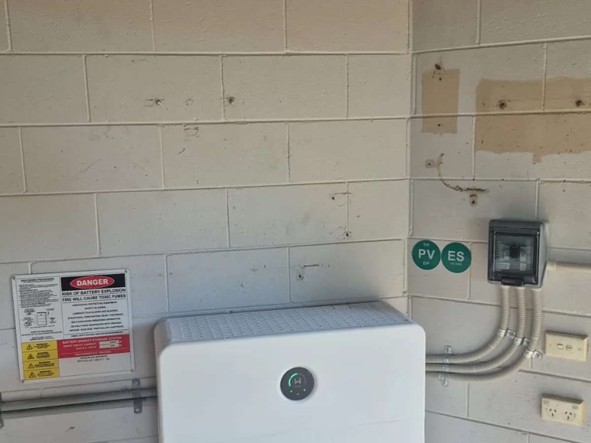 A home battery installed by EFS Solar against a painted block wall in Smithfield, beside the isolators and shutdown signage