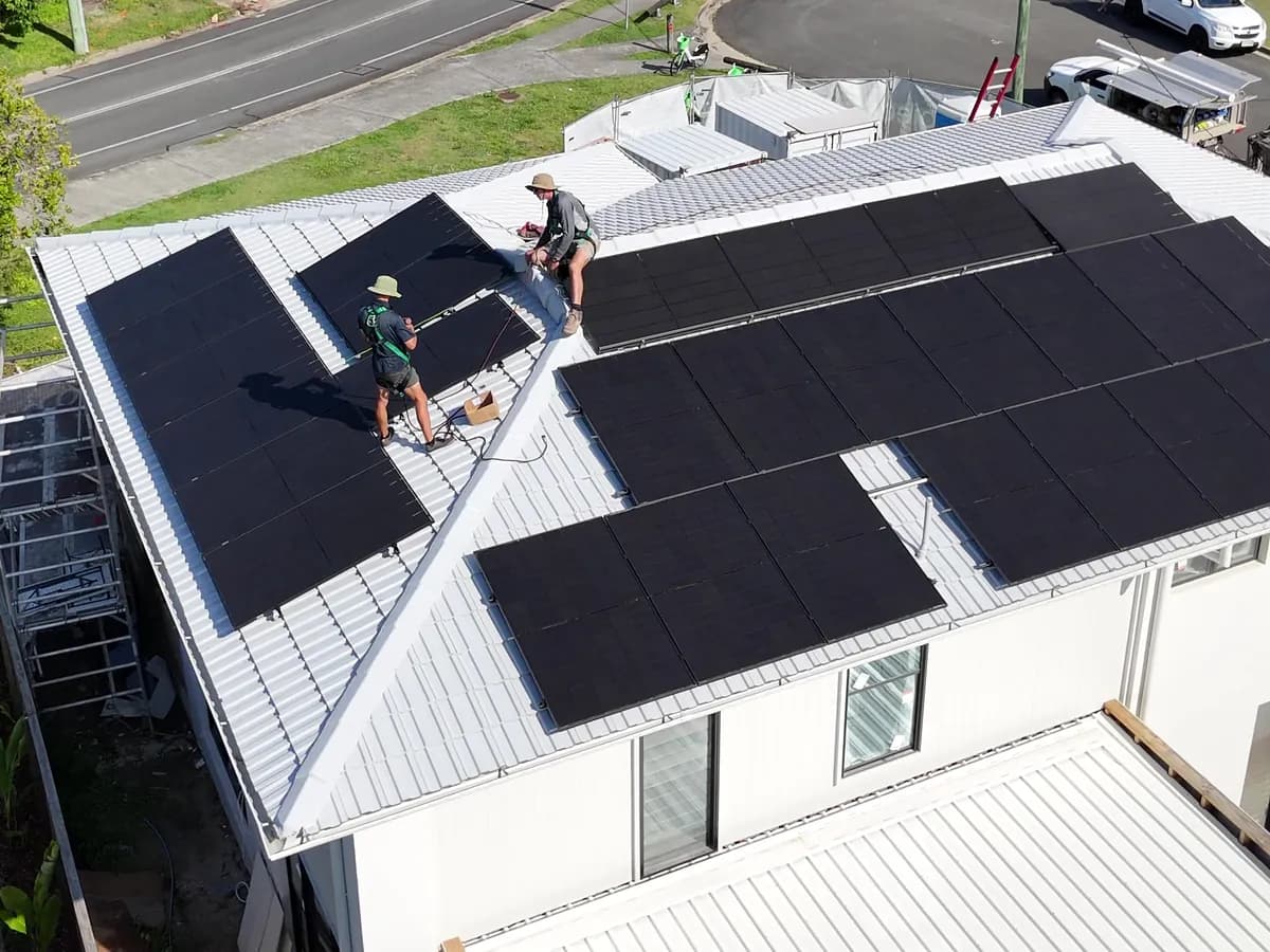 Solar installation in Southport — installers fitting black panels to a white metal roof, with the Surfers Paradise skyline behind