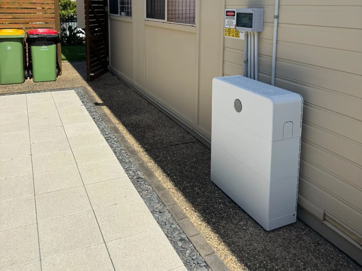A home battery installed by EFS Solar along the weatherboard wall of a Springfield home, with the isolator and shutdown signage above