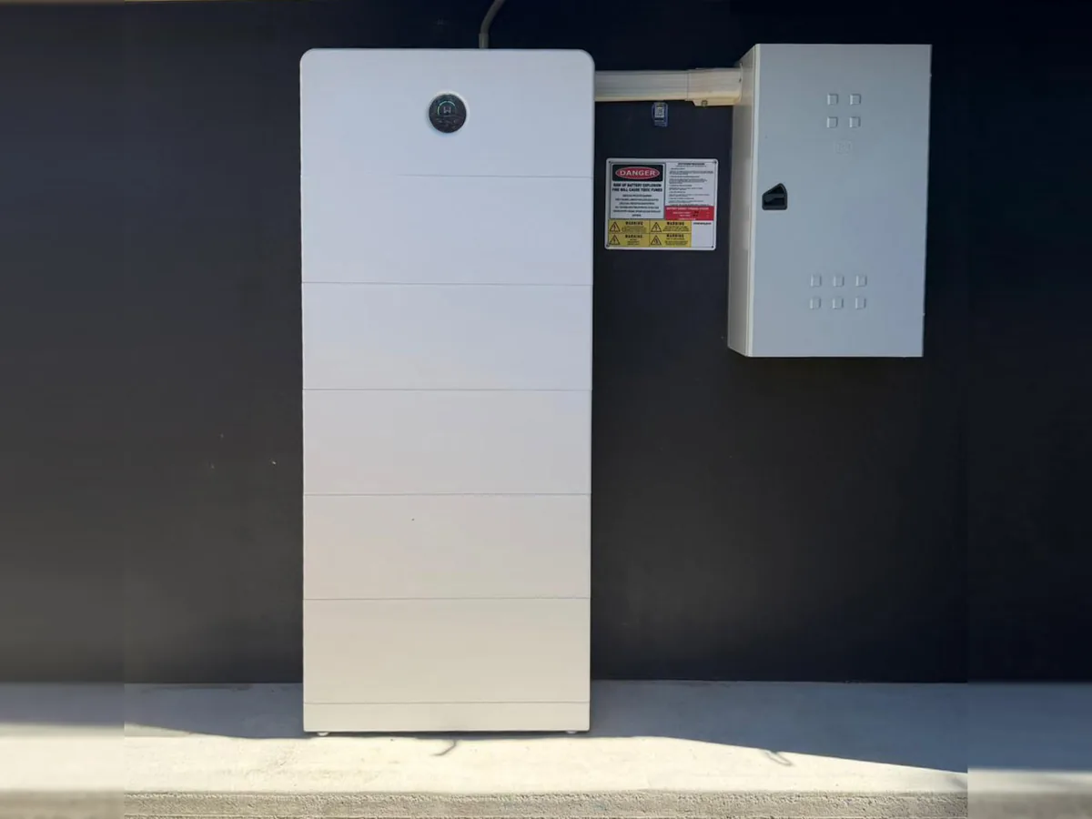 A tall home battery installed by EFS Solar against a dark rendered wall in Victoria Point, with the switchboard and shutdown signage beside it