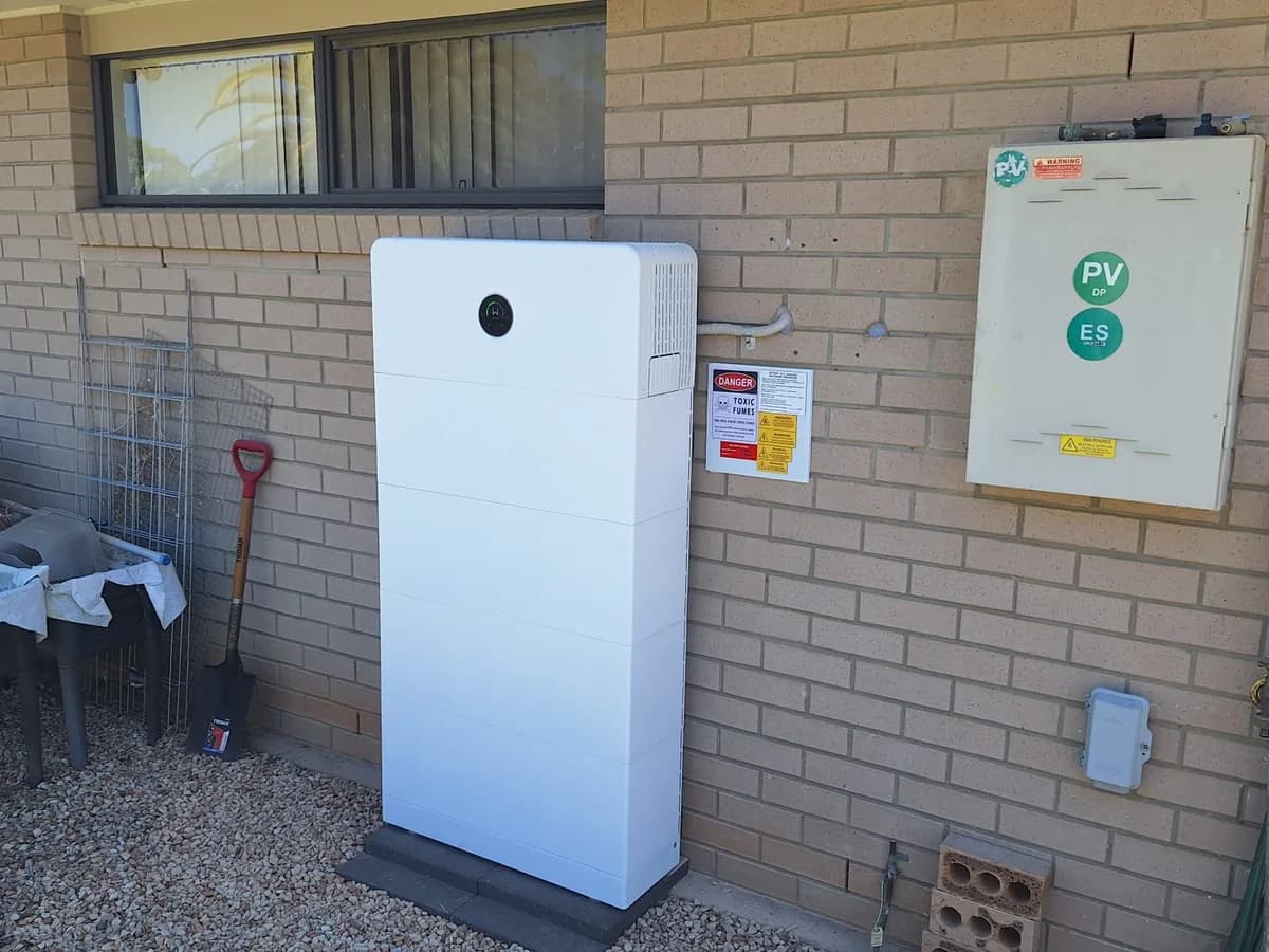 A home battery installed by EFS Solar against a brick wall in Wamuran, beside the meter box and garden