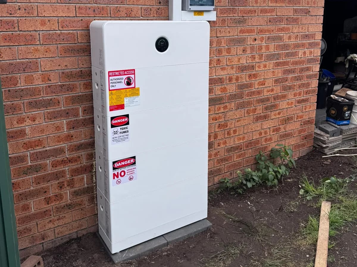 A home battery installed by EFS Solar against a brick wall at a Wattle Grove home, with restricted-access and shutdown signage