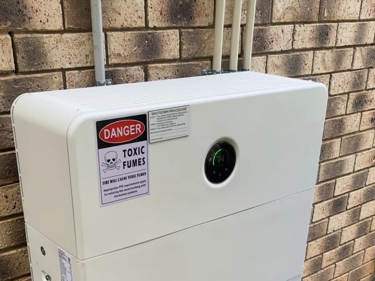A home battery installed by EFS Solar against a brick wall in Wellington Point, with the switchboard and shutdown signage above