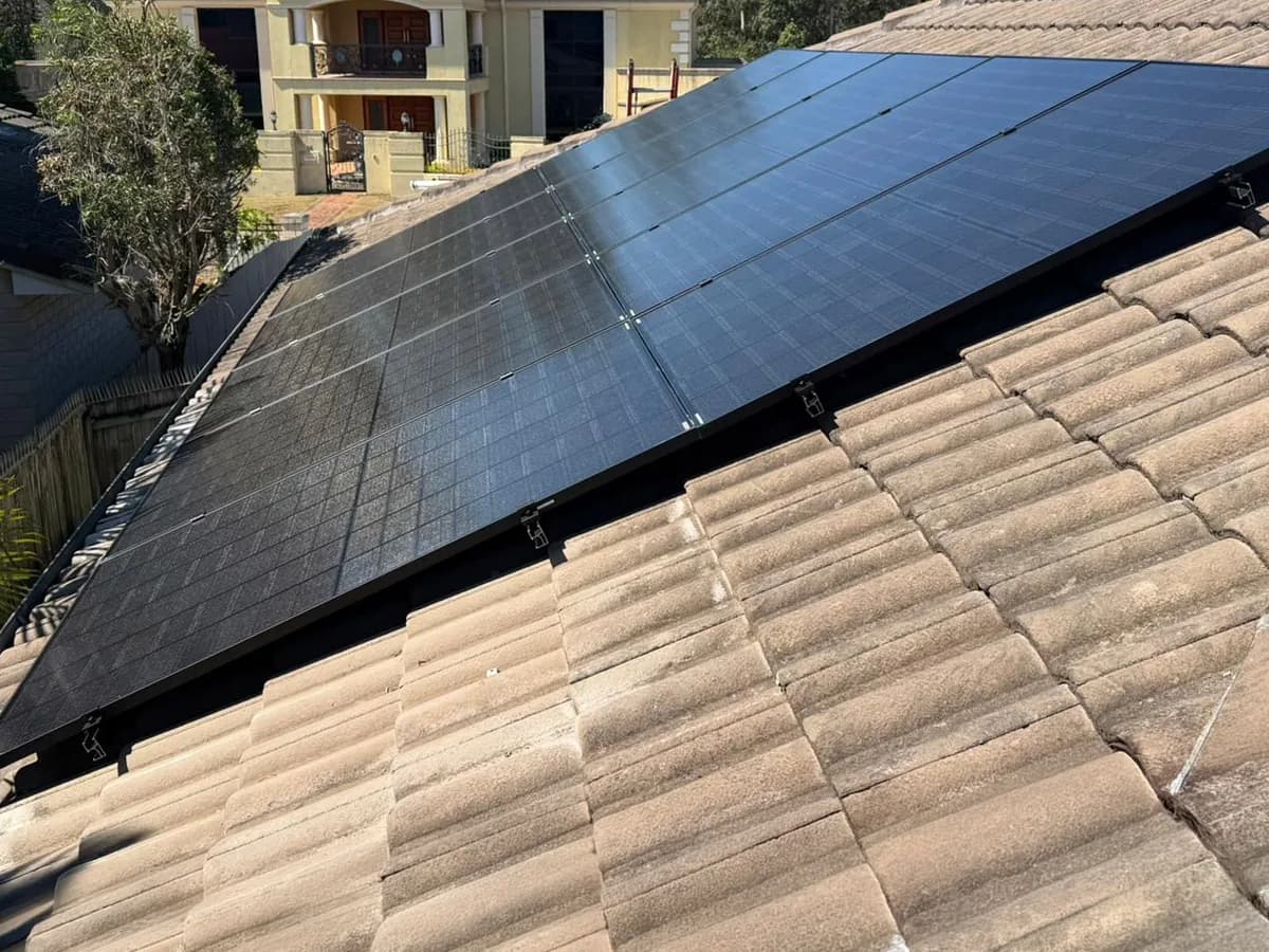 Black solar panels fitted to a terracotta-tiled roof in Westlake, with neighbouring homes behind